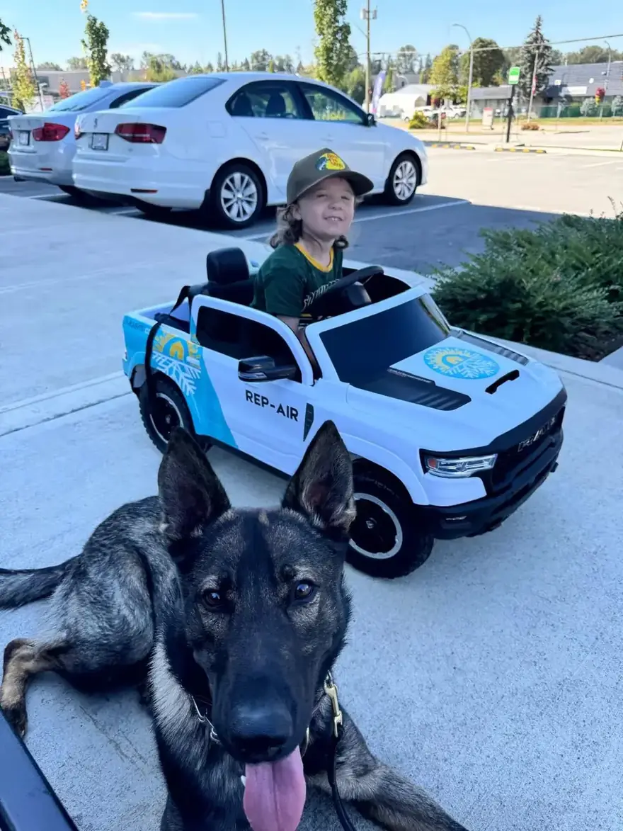 Child in a toy Rep-Air truck next to a dog