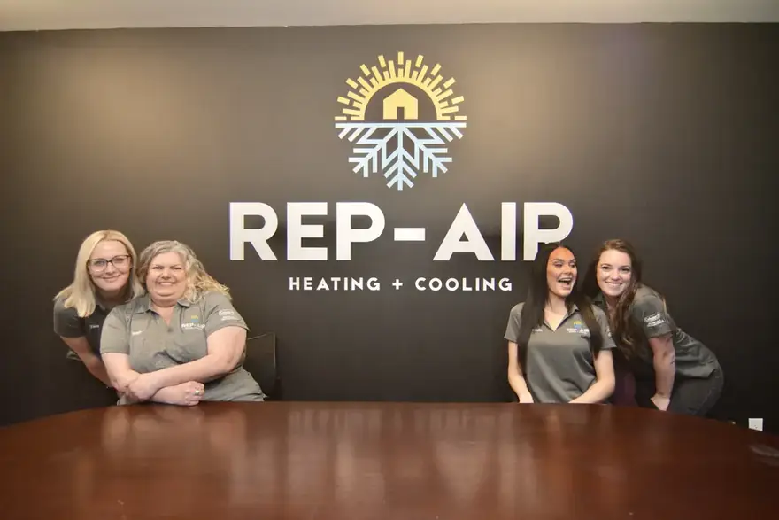 Rep-Air office team in front of the logo wall