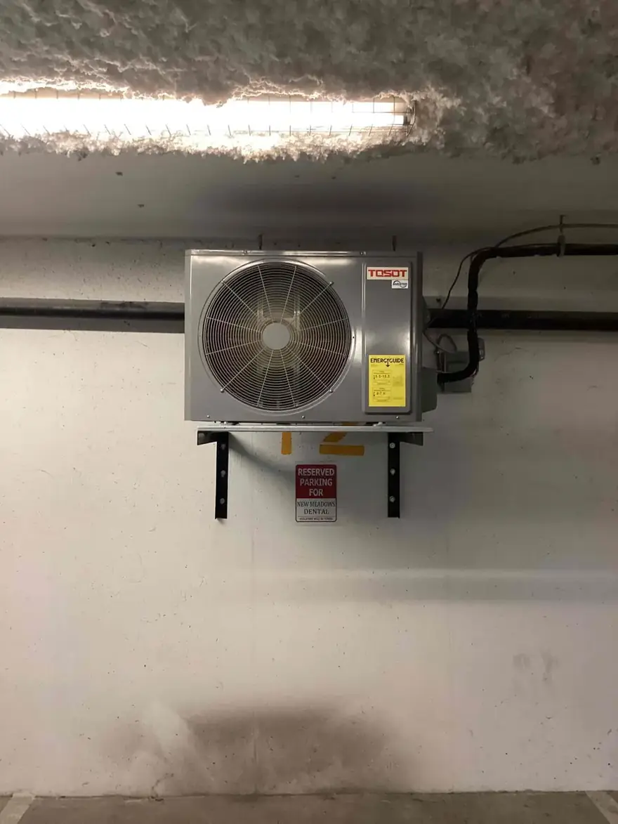 Heat pump outdoor unit on wall brackets in a parkade