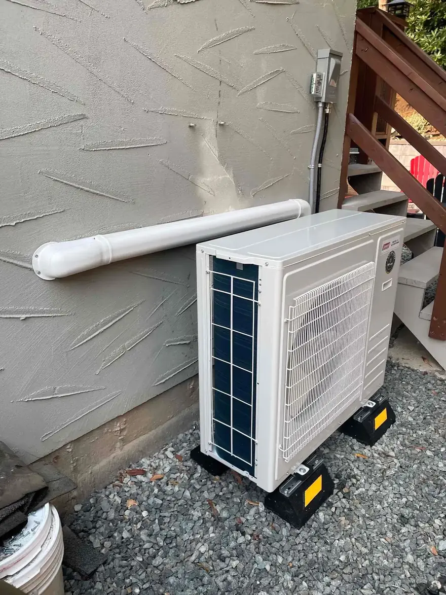 Heat pump outdoor unit on risers beside a stucco wall