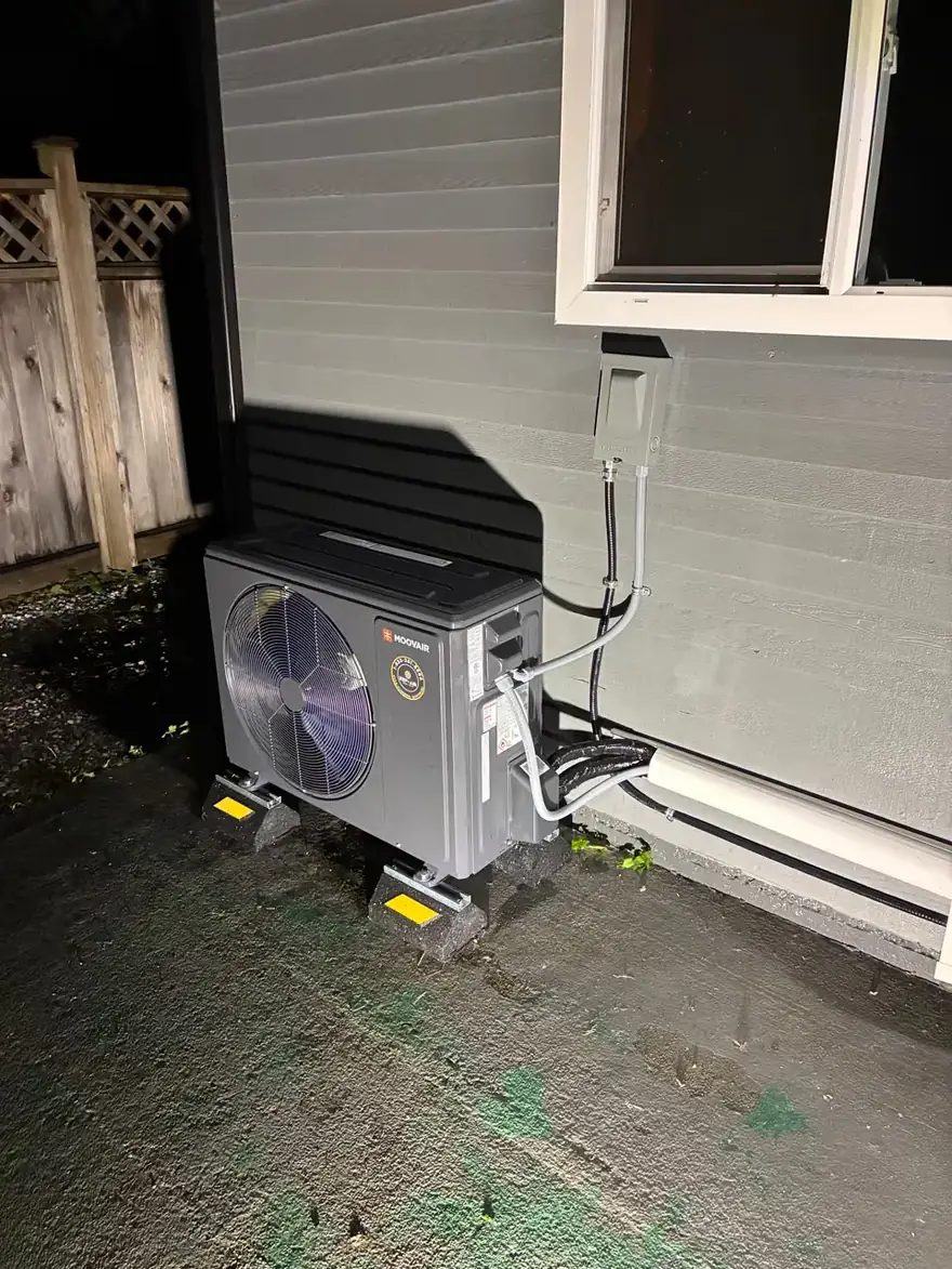 Ductless heat pump outdoor unit on a stand beside a house