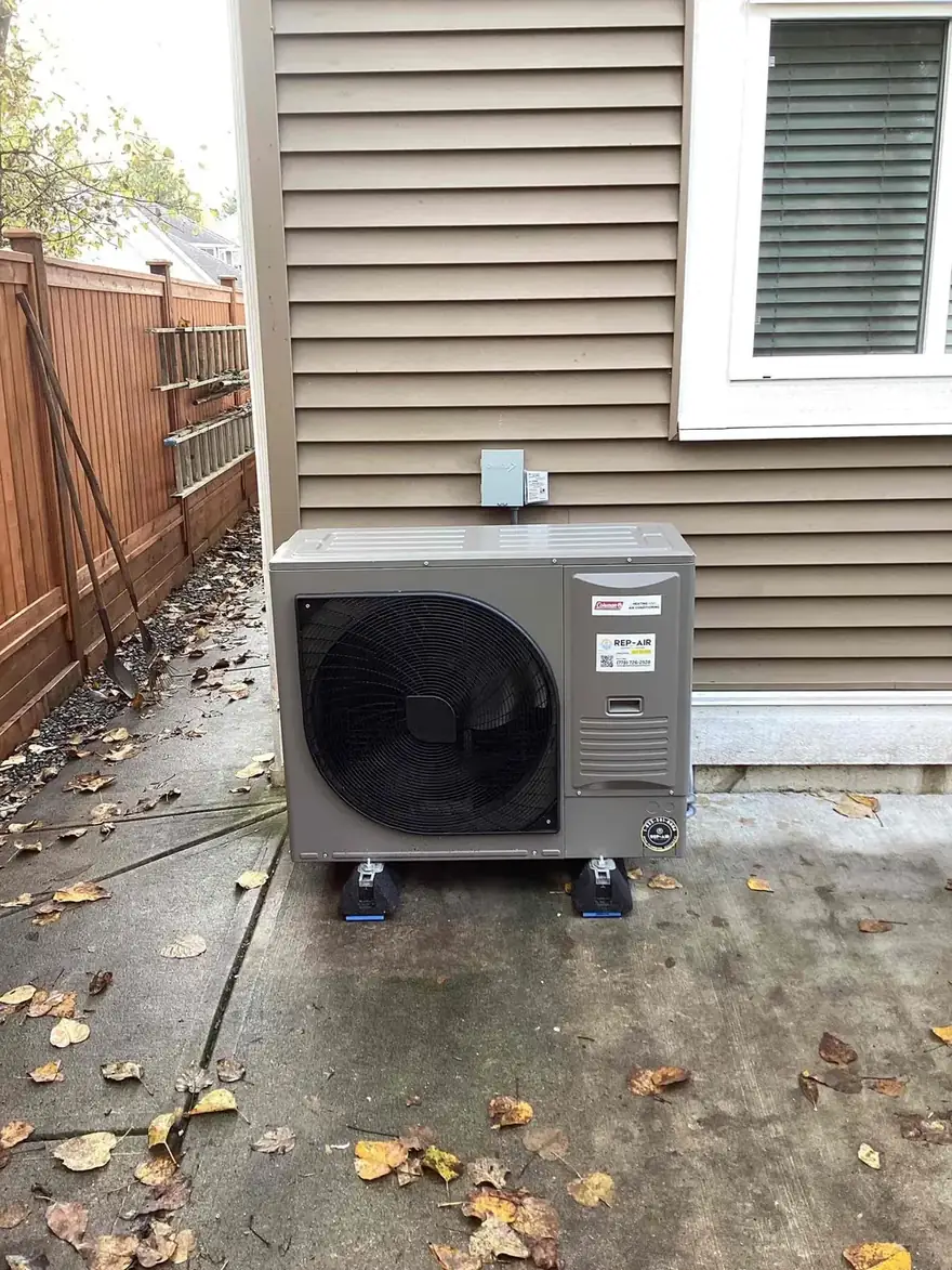 Heat pump outdoor unit on risers beside a house in the fall