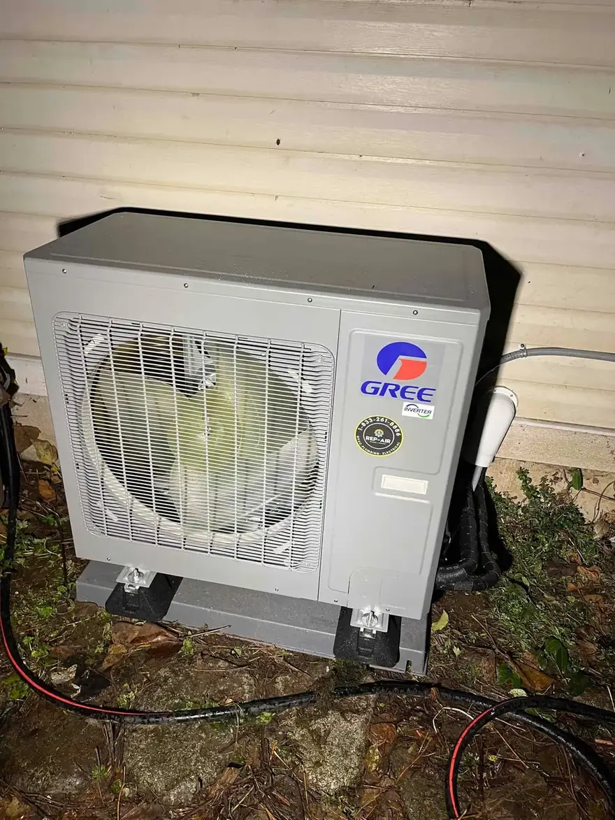 Gree heat pump outdoor unit beside a house at night