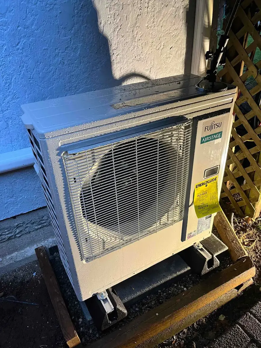 Fujitsu heat pump outdoor unit on a stand beside a stucco wall