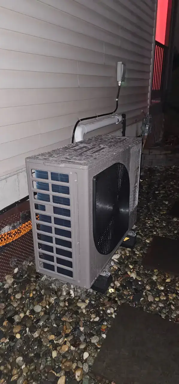 Heat pump outdoor unit on a gravel bed beside vinyl siding