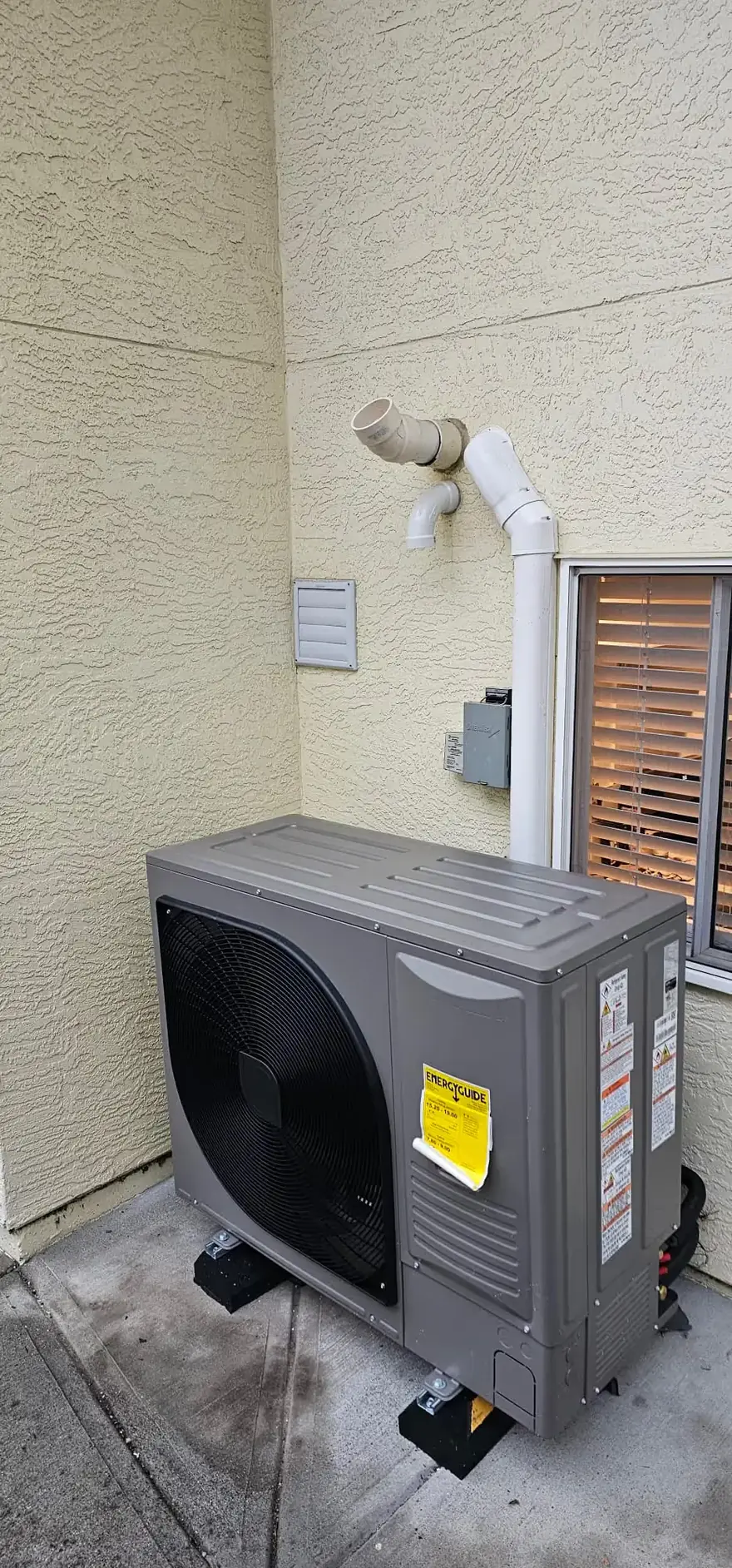 Heat pump outdoor unit on a pad beside a stucco wall