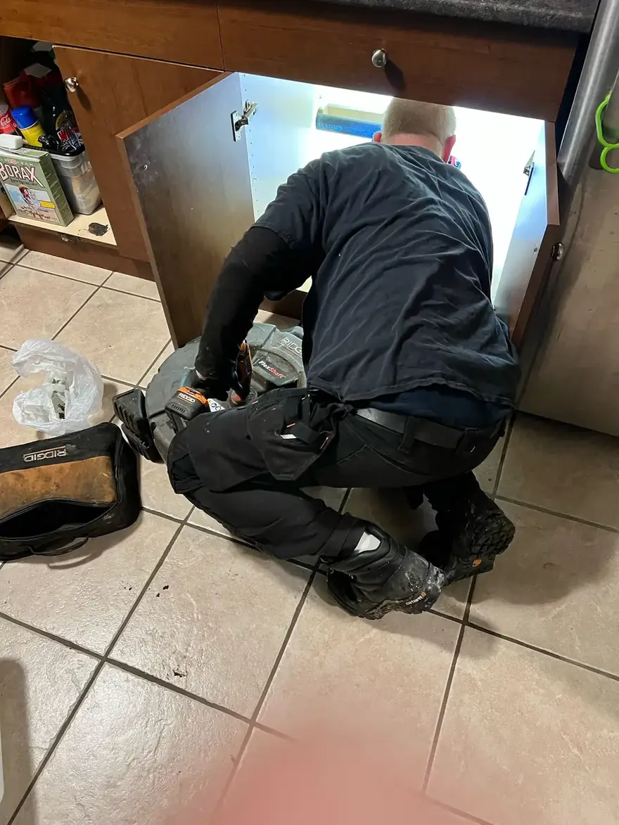 Technician kneeling to work under a kitchen cabinet