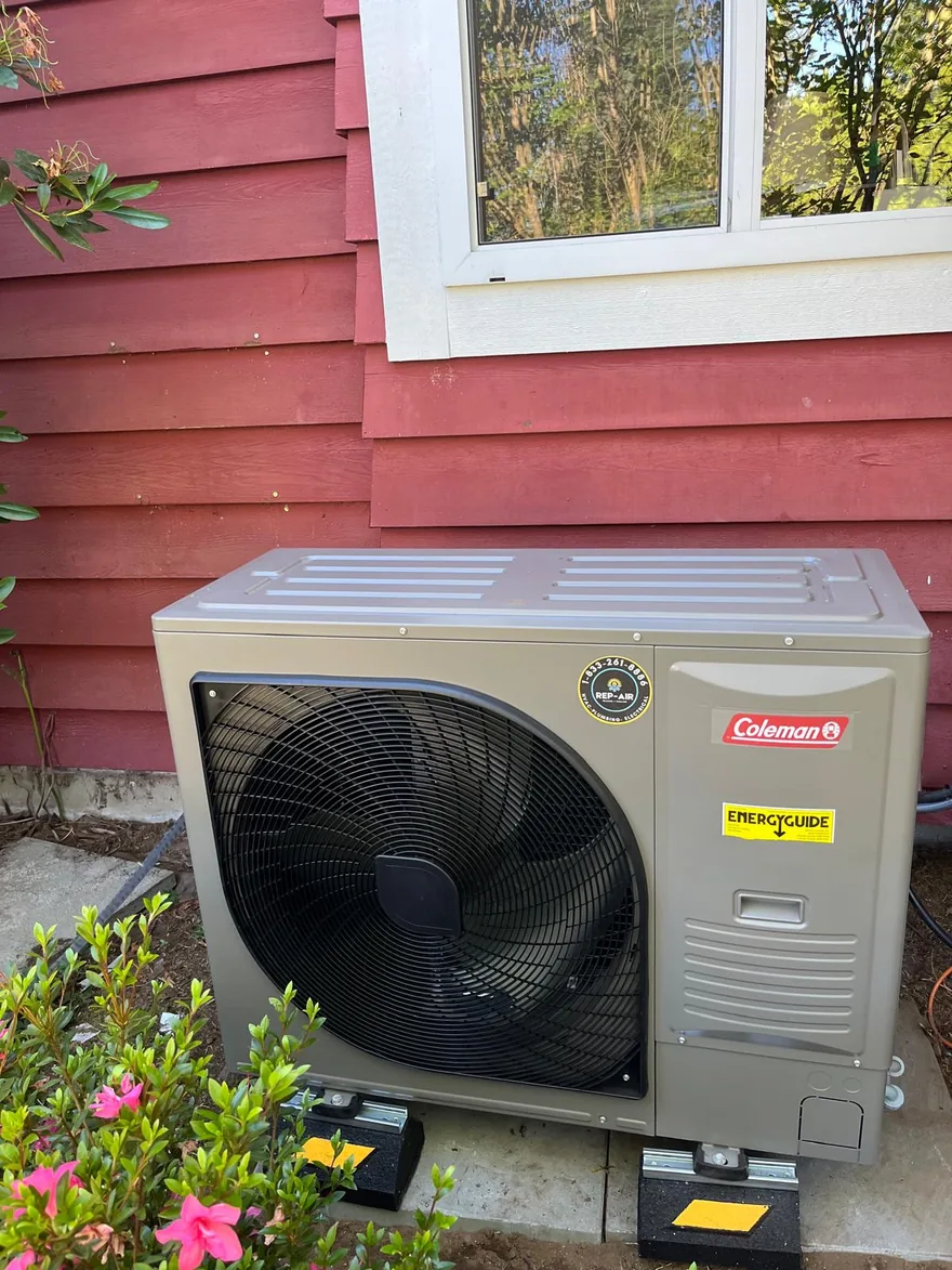 Coleman heat pump outdoor unit beside a red house