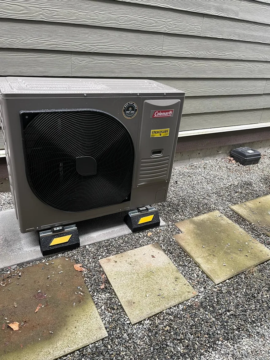 Coleman heat pump outdoor unit on risers beside a house