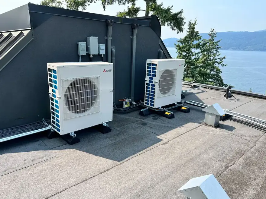 Two ductless heat pump outdoor units on a flat roof by the water